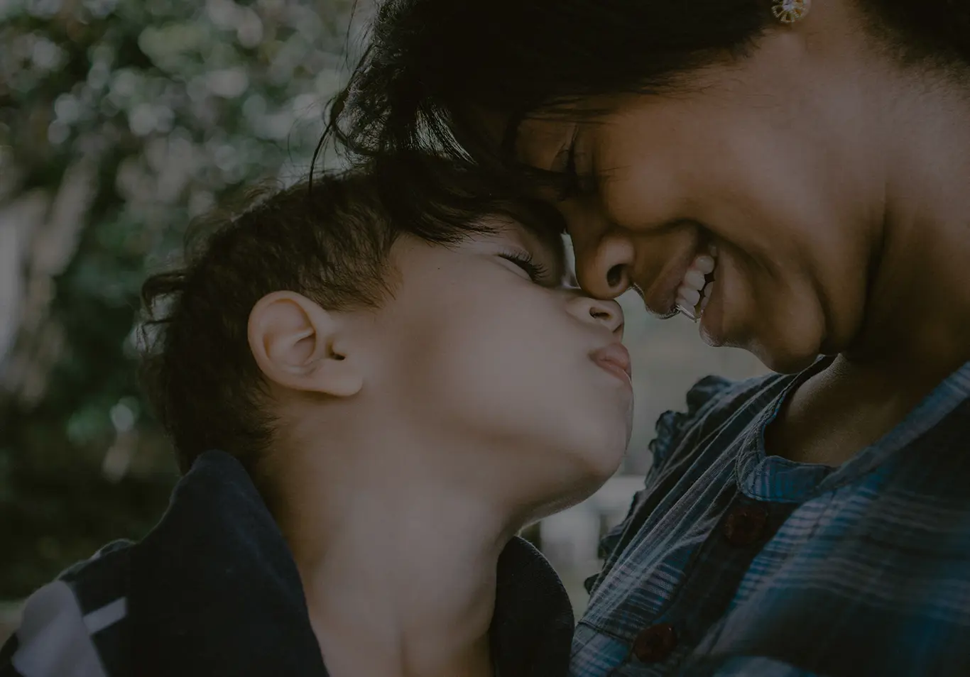Close up of woman and child touching noses and smiling with closed eyes.