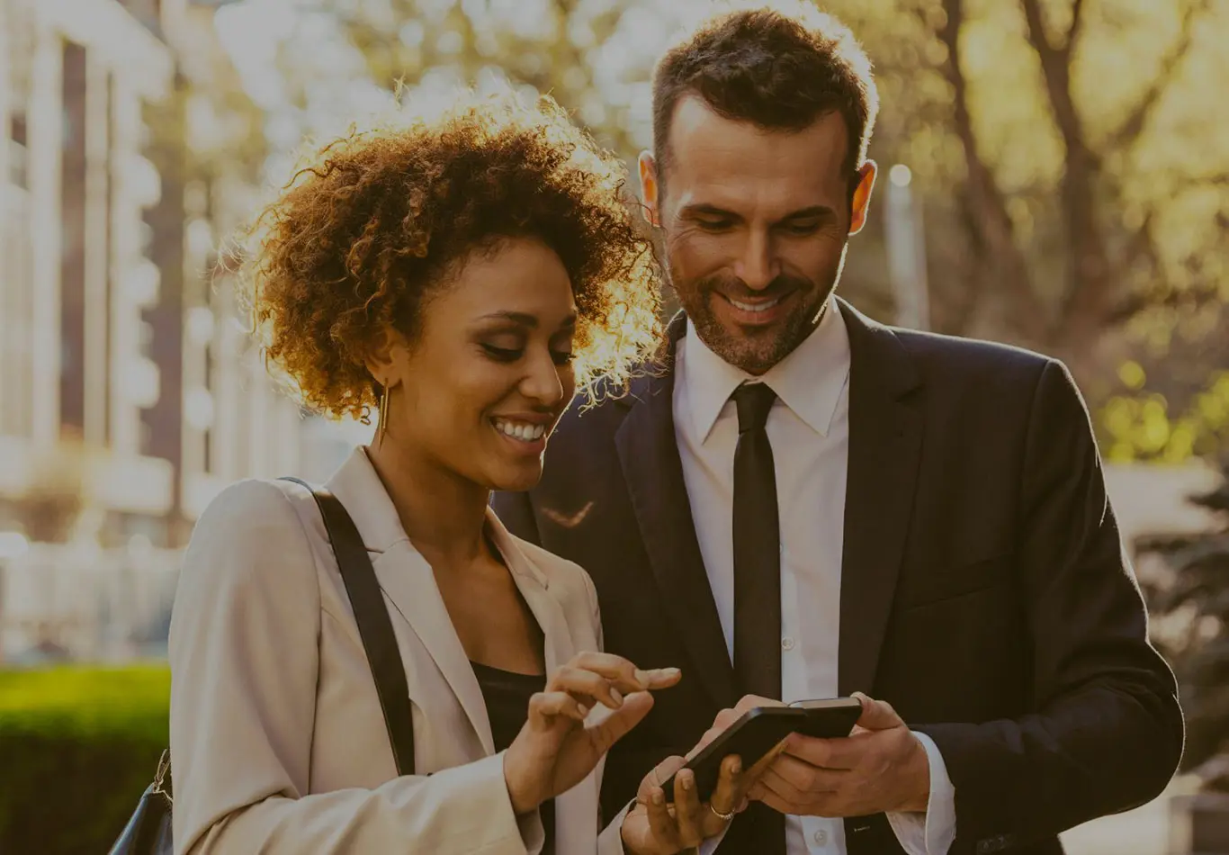 Market Key Benefits 2 A business man and business woman are standing next to each other on the street. They are looking at their phones.