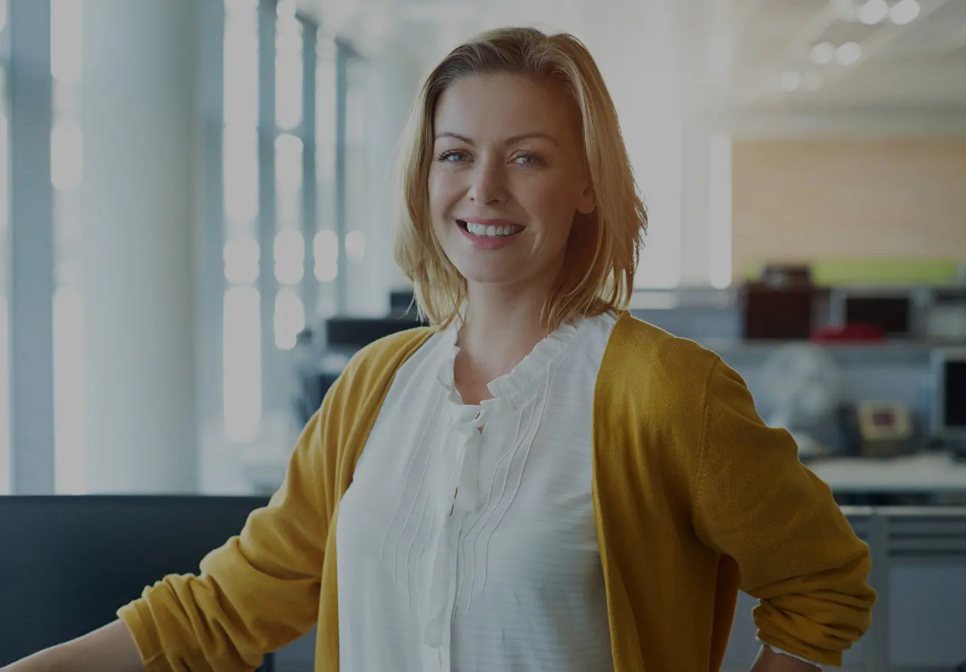 Market Key Benefits 3 A blonde haired business woman in a white blouse and yellow cardigan is looking at the viewer.