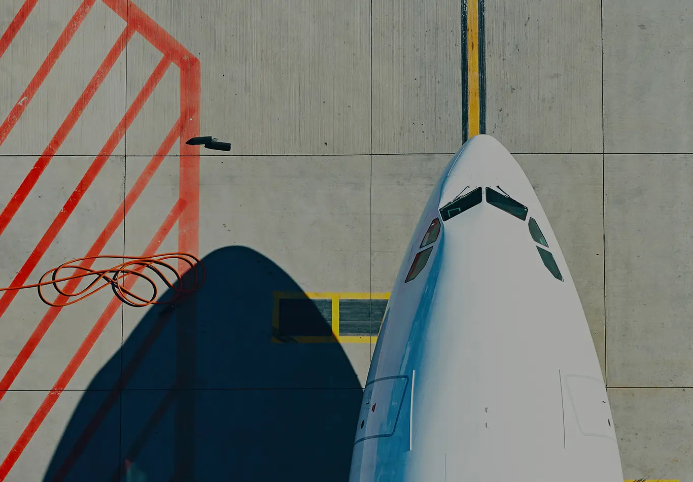 Arial view of the nose of an airplane about to take off, there are red and yellow directional lines on the ground below the plane. 